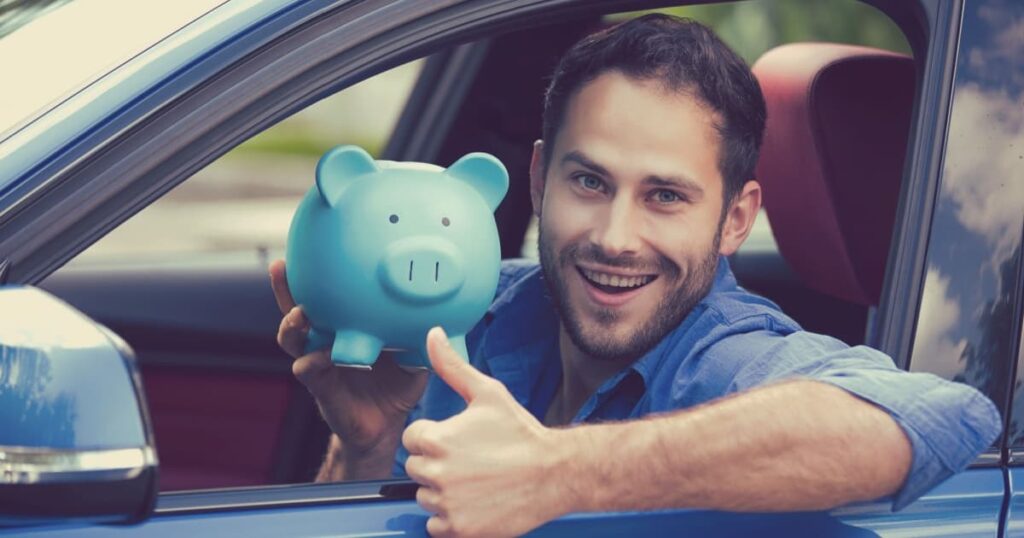 homme heureux dans une voiture qui lève un pouce en l'air en tenant un cochon tirelire bleu 