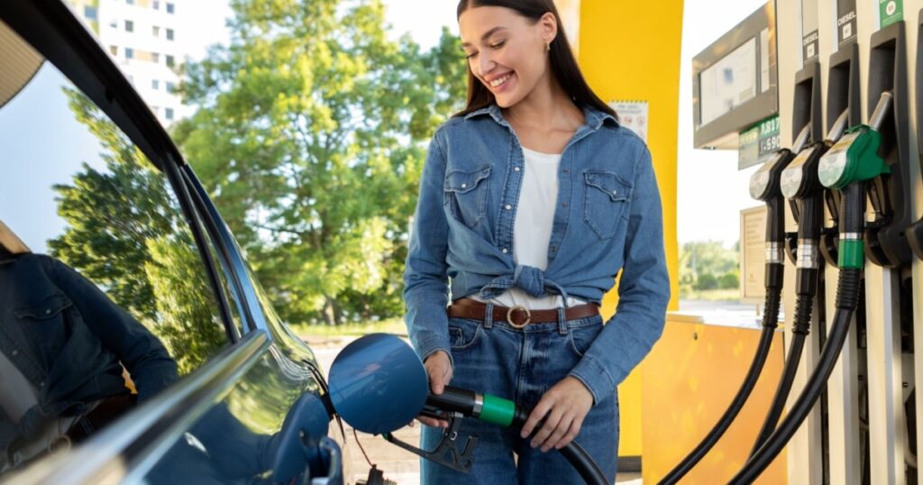 Une jeune femme faisant le plein de sa voiture à une station-service. 