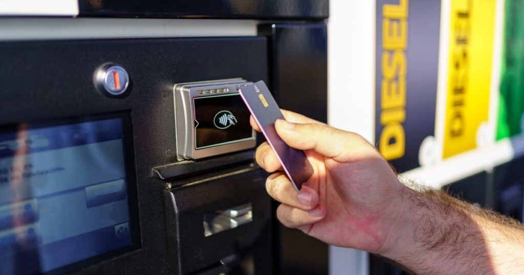 Une main d'homme tient une carte de paiement devant le terminal d'une borne de station-service. 